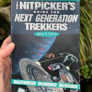 May include: A paperback book titled "The Nitpicker's Guide for Next Generation Trekkers, part two." The cover features a spaceship illustration against a dark blue space background. Text includes "Unauthorized! Unabridged! Uncensored!" and actor names.