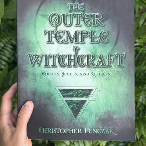 Pode incluir: Um livro intitulado "The Outer Temple of Witchcraft" com uma capa verde e preta. A capa apresenta o t&iacute;tulo em letras grandes e ornamentadas, com o nome do autor, Christopher Penczak, na parte inferior. O subt&iacute;tulo do livro &eacute; "C&iacute;rculos, Feiti&ccedil;os e Rituais."