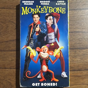 May include: A VHS tape of the movie Monkeybone featuring Brendan Fraser, Bridget Fonda, and Chris Kattan on the cover. The artwork displays two men standing behind a cartoon monkey holding two bananas, with the text Monkeybone and Get Boned!