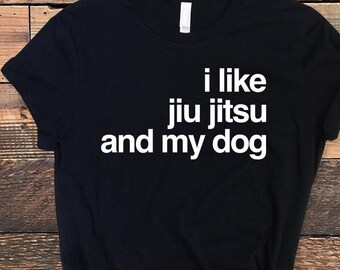May include: A black short-sleeved t-shirt featuring white text printed on the front that reads, "i like jiu jitsu and my dog." The garment has a crew neckline and a standard fit, showcasing a simple design with bold, legible lettering.