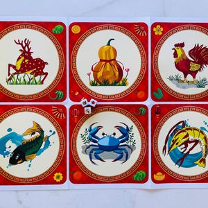 Puede incluir: Seis tarjetas cuadradas rojas y blancas con un borde dorado y una imagen circular en el centro. Las imágenes son de un ciervo, una calabaza, un gallo, un pez, un cangrejo y un camarón. Cada imagen está rodeada por un borde dorado y un patrón rojo y blanco.
