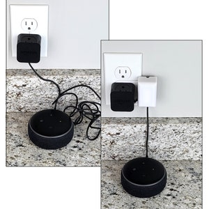 May include: Two black Amazon Echo Dot smart speakers plugged into white electrical outlets with black power adapters. The speakers are on a granite countertop.