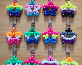 May include: A collection of star-shaped keychains, each crafted from colorful beads. The keychains feature various pride flag color schemes, including rainbow, pink, blue, and yellow. Each keychain has a silver-colored clasp for easy attachment.