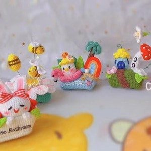 Puede incluir: Una colección de juguetes amigurumi de crochet coloridos, que incluyen un conejito en una maceta de flores, un dragón, una nube, un flamenco y un caracol. Los juguetes están hechos a mano y presentan detalles intrincados.
