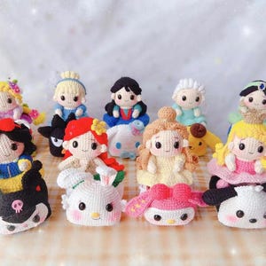 Puede incluir: Una colección de diez muñecas de crochet, cada una con un diseño y una combinación de colores diferente. Las muñecas están vestidas con diferentes atuendos, que incluyen vestidos, faldas y pantalones. Algunas de las muñecas sostienen accesorios, como flores, varitas y bolsos. Todas las muñecas están sentadas sobre una superficie blanca.