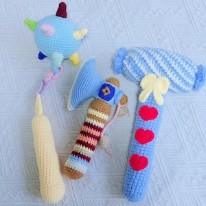 May include: A collection of three handmade crochet toys in various shapes and colors. One is a blue and yellow star-shaped toy with a dangling string. Another is a blue axe with a brown and striped handle. The third is a blue hammer with red hearts.