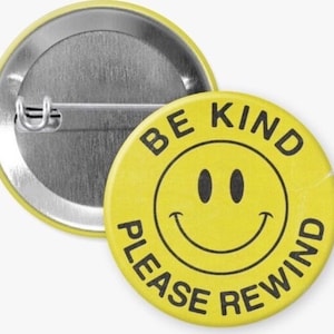 May include: Yellow button with a black smiley face and the text "Be Kind Please Rewind" in black.