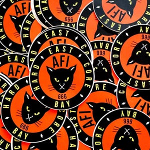 May include: A collection of round stickers with a black cat graphic, the text "East Bay AFI Hard Core 666" and a diamond pattern. The stickers are orange with black lettering and a black border.