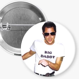 May include: A white button with a photo of a man wearing sunglasses and a white t-shirt with the text "BIG DADDY" printed on it.