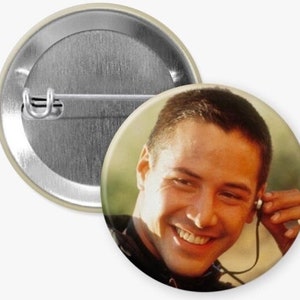 May include: A close-up portrait of a man with short brown hair smiling. He is wearing a black shirt and has an earbud in his ear.