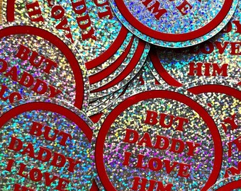 May include: A collection of round stickers with a red border and the text "BUT DADDY I LOVE HIM" in red. The stickers have a holographic, glittery background, creating a shimmering effect. The stickers are scattered across the image.