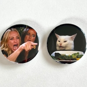 Puede incluir: Dos botones redondos con imágenes de memes de internet populares. El primer botón muestra a una mujer gritándole a un gato, y el segundo botón muestra a un gato mirando un plato de comida con una expresión de disgusto. El texto en el primer botón dice "Woman yelling at cat".