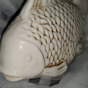May include: White ceramic fish figurine with brown scales and a detailed eye. The fish has a smooth, glossy finish.