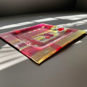 May include: Square glass tray with a red and gold geometric pattern. The tray is made of clear glass with a textured surface.