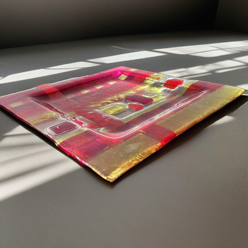 May include: Square glass tray with a red and gold geometric pattern. The tray is made of clear glass with a textured surface.