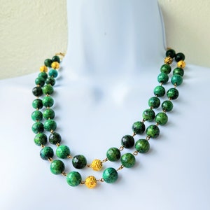 May include: A double strand necklace made of green gemstone beads with gold accents. The beads are round and have a faceted finish.