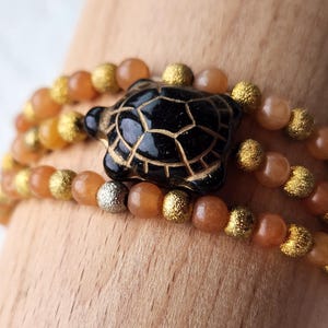 May include: A multi-strand bracelet with brown and gold beads and a black turtle charm.