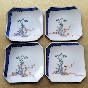 May include: Set of four square ceramic plates. Each plate features a white surface with a blue wave pattern border. A central design depicts a tree with green leaves and red flowers. The plates are ideal for serving appetizers or small dishes.