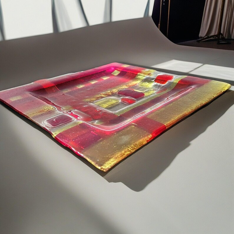 May include: A square glass serving tray with a red and gold checkered pattern. The tray is made of clear glass with red and gold stripes.