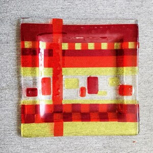 May include: A rectangular glass serving dish with a red and yellow geometric pattern. The dish has a checkered pattern in the centre and stripes around the edges.