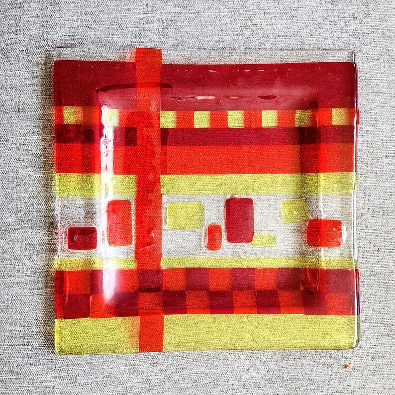 May include: A rectangular glass serving dish with a red and yellow geometric pattern. The dish has a checkered pattern in the centre and stripes around the edges.