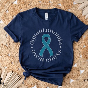 May include: Navy blue t-shirt featuring a teal ribbon and the text "dysautonomia awareness" in a circle around the ribbon.