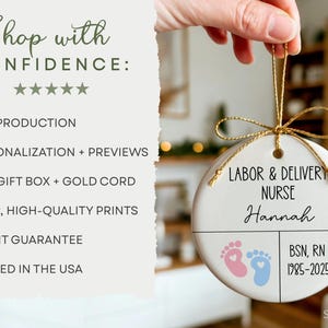 K&ouml;nnte beinhalten: Ein wei&szlig;es Keramikornament mit einer goldenen Kordel, mit dem Text "LABOR & DELIVERY NURSE Hannah" und Babyf&uuml;&szlig;en. Das Ornament enth&auml;lt auch den Text "BSN, RN 1985-2025".