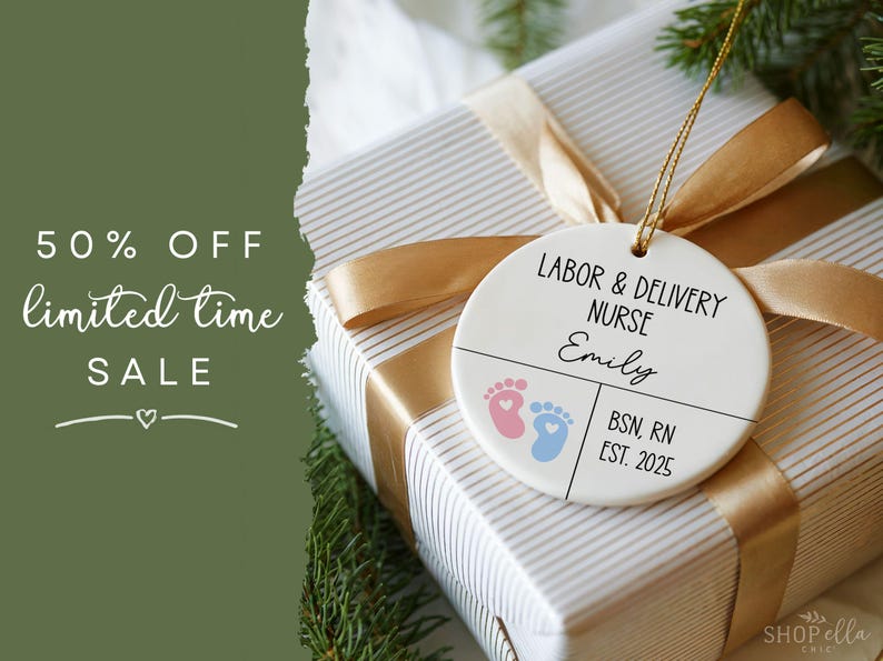 K&ouml;nnte beinhalten: Ein runder, wei&szlig;er Ornament mit dem Text "LABOR & DELIVERY NURSE" und "Emily". Es zeigt rosa und blaue Babyf&uuml;&szlig;e und den Text "BSN, RN EST. 2025". Der Ornament h&auml;ngt an einem goldenen Band &uuml;ber einem verpackten Geschenk.
