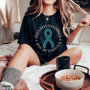 May include: A black t-shirt with a teal ribbon and the text "Dysautonomia Awareness" in a circle.