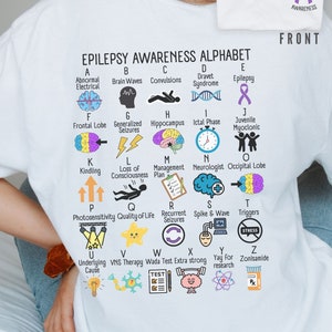 May include: White t-shirt with a purple epilepsy awareness ribbon on the front and an alphabet chart on the back. The chart features illustrations and definitions of terms related to epilepsy.