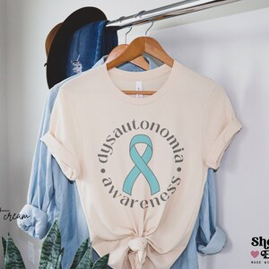 May include: A cream coloured t-shirt with a teal ribbon and the text "dysautonomia awareness" in a circle.