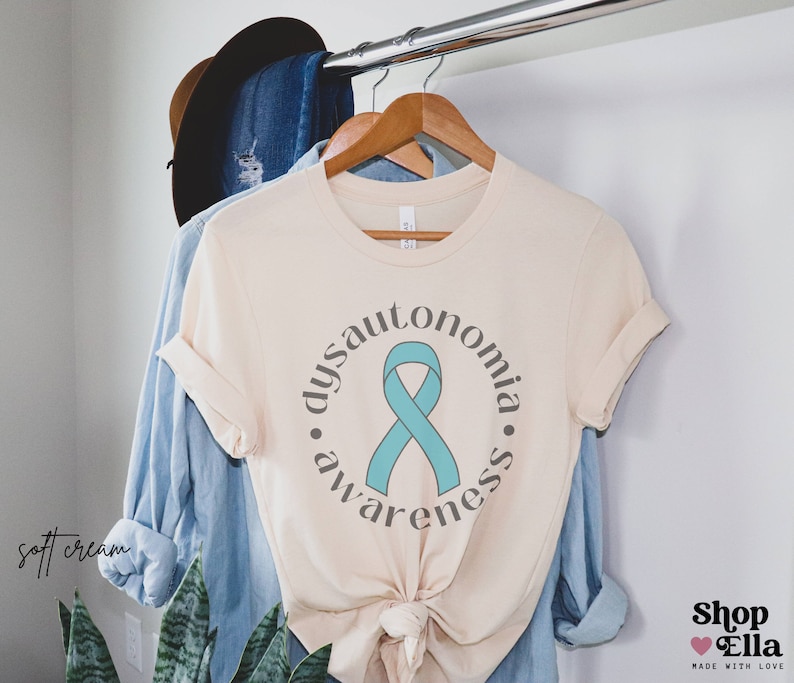 May include: A cream coloured t-shirt with a teal ribbon and the text "dysautonomia awareness" in a circle.