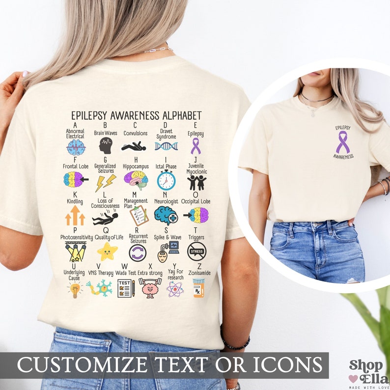 May include: A light beige t-shirt with a purple ribbon and the text "Epilepsy Awareness" on the front. The back of the shirt features an alphabet chart with illustrations and text related to epilepsy. The text on the chart includes terms like "Abnormal Electrical", "Brain Waves", "Convulsions", "Dravet Syndrome", "Epilepsy", "Frontal Lobe", "Generalized Seizures", "Hippocampus", "Ictal Phase", "Juvenile Myoclonic", "Kindling", "Loss of Consciousness", "Management Plan", "Neurologist", "Occipital Lobe", "Photosensitivity", "Quality of Life", "Recurrent Seizures", "Spike & Wave", "Triggers", "Underlying Cause", "VNS Therapy", "Wada Test", "Extra Strong", "Yay for Research", and "Zonisamide".