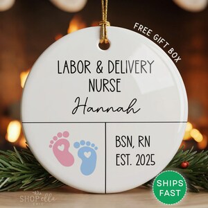 Round ceramic ornament with white background featuring pink and blue baby footprints. Text reads Labor and Delivery Nurse with custom name, credentials, and year. Includes Free Gift Box and Ships Fast.