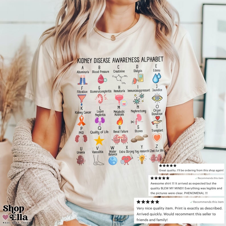 May include: A white t-shirt with a colorful alphabet chart about kidney disease awareness. Each letter of the alphabet is paired with a related term and a corresponding illustration. The shirt has the text "KIDNEY DISEASE AWARENESS ALPHABET" at the top.