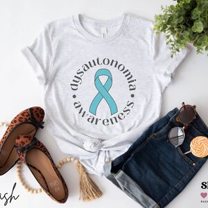 May include: A white t-shirt with a teal ribbon and the text "dysautonomia awareness" in a circle around the ribbon.