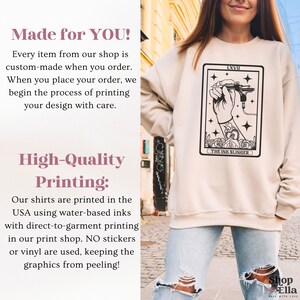 Puede incluir: Una sudadera beige con una ilustraci&oacute;n en blanco y negro de una mano sosteniendo una m&aacute;quina de tatuaje. La ilustraci&oacute;n est&aacute; rodeada por un borde negro y el texto "LXVII THE INK SLINGER".