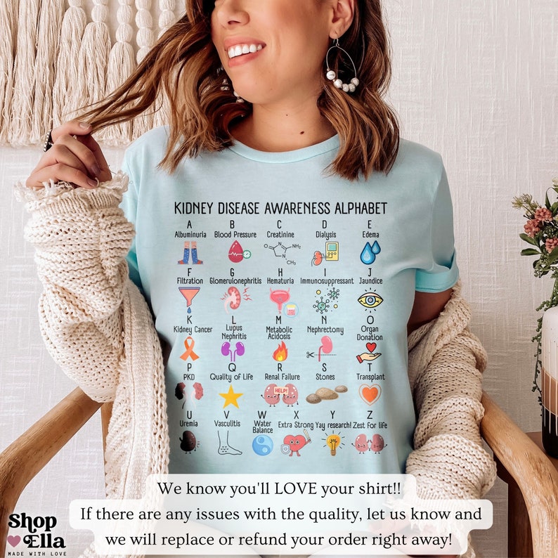 May include: A light blue t-shirt with a graphic of an alphabet representing kidney disease awareness. The graphic features icons and text for each letter of the alphabet. The text on the shirt reads "Kidney Disease Awareness Alphabet".