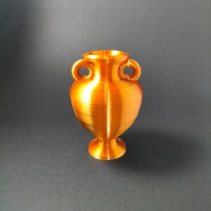May include: A small, golden, ceramic vase with two handles. The vase has a smooth, shiny finish and a rounded body.