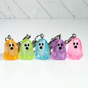 May include: Five colorful ghost keychains in orange, green, blue, purple, and pink. Each ghost has a black face and a silver keychain attachment. The ghosts are translucent and have a glossy finish.