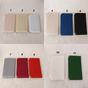 Pu&ograve; includere: Una collezione di undici oggetti rettangolari rivestiti in tessuto, ciascuno dotato di angolari di protezione in metallo dorato. Gli oggetti sono presentati in vari colori, tra cui rosa cipria, beige, azzurro, crema, blu, nero, grigio, bordeaux, rosso, bianco e verde.