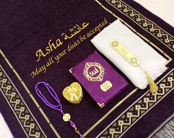 May include: A deep purple prayer mat with gold detailing and the name "Asha" embroidered in gold. Includes a small purple Quran, a white scarf, a heart-shaped box, and a purple beaded rosary.