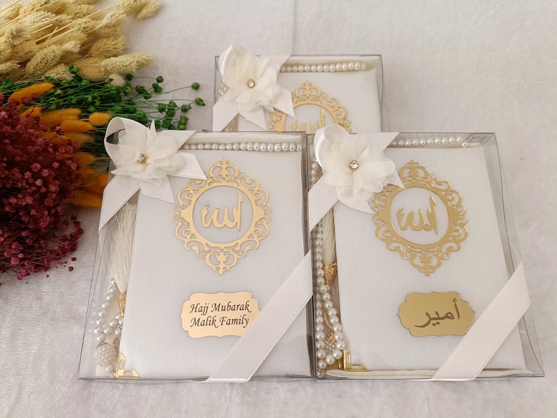 Pu&ograve; includere: Tre scatole regalo bianche contenenti set da preghiera, ciascuna con un emblema in calligrafia araba dorata, un fiore in tessuto bianco con uno strass centrale, un rosario di perle bianche e una targhetta dorata personalizzata.