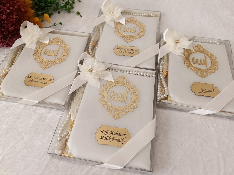 Pu&ograve; includere: Quattro scatole regalo bianche contenenti libri di preghiera e grani di preghiera in perla. Ogni scatola presenta una cornice in filigrana dorata con calligrafia araba, un fiore in tessuto bianco, un nastro bianco e una targhetta dorata.