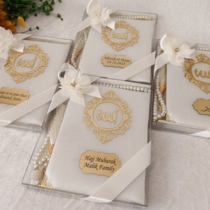 Pu&ograve; includere: Quattro scatole regalo bianche contenenti libri di preghiera e grani di preghiera in perla. Ogni scatola presenta una cornice in filigrana dorata con calligrafia araba, un fiore in tessuto bianco, un nastro bianco e una targhetta dorata.