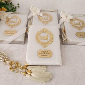 Pu&ograve; includere: Quattro scatole regalo rettangolari bianche contenenti libri di preghiera, decorate con una cornice in filigrana dorata con la parola araba per Allah. Ogni scatola include un nastro di raso bianco, un fiore bianco e una targhetta dorata personalizzata.