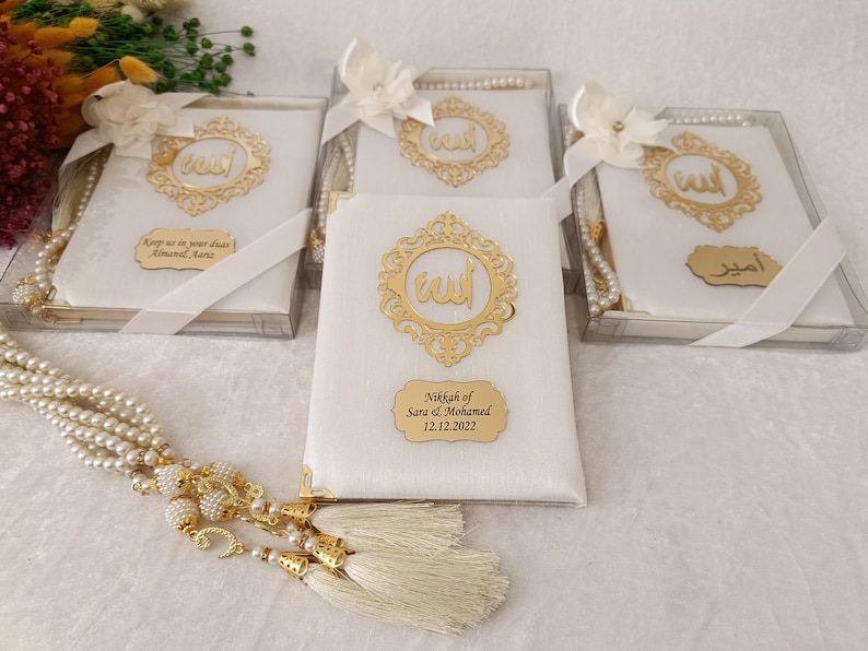 Pu&ograve; includere: Quattro scatole regalo rettangolari bianche contenenti libri di preghiera, decorate con una cornice in filigrana dorata con la parola araba per Allah. Ogni scatola include un nastro di raso bianco, un fiore bianco e una targhetta dorata personalizzata.
