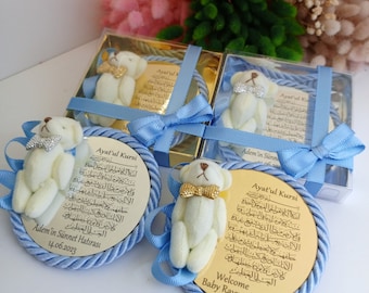 May include: Four circular gold-toned plaques featuring the Ayat'ul Kursi prayer in Arabic script, each adorned with a small cream-colored teddy bear wearing a glittery bow tie. The plaques are framed by blue twisted rope and blue ribbon bows.