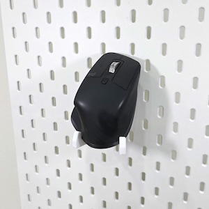 Op de afbeelding: Een zwarte draadloze computermuis met een scrollwiel en knoppen is met een witte houder op een wit pegboard gemonteerd. De muis is iets naar rechts gekanteld.