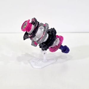 May include: A multi-colored toy with a white base. The toy features a pink, black, and gray design with a purple tip. The toy is designed with multiple layers and a circular shape. The toy is designed to spin.